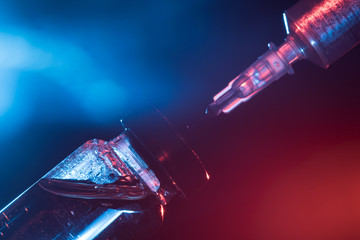 A glass medical bottle with a vaccine and a disposable syringe in color light. A conceptual photo...