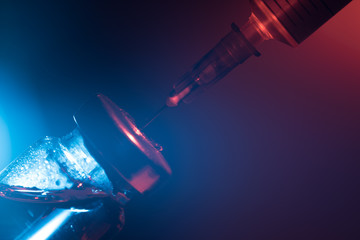 A glass medical bottle with a vaccine and a disposable syringe in color light. A conceptual photo about the danger of viral diseases.