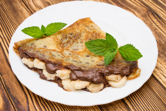 Crepes with bananas and cream on a wooden background