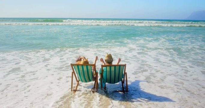 Rear view of active senior Caucasian couple relaxing on a sun lounger at beach 4k