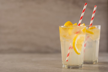 two glass of lemonade with lemons and lime and straw, on a dark background, with space, a cool drink and summer mood