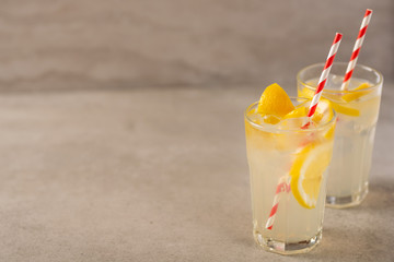 two glass of lemonade with lemons and lime and straw, on a dark background, with space, a cool drink and summer mood