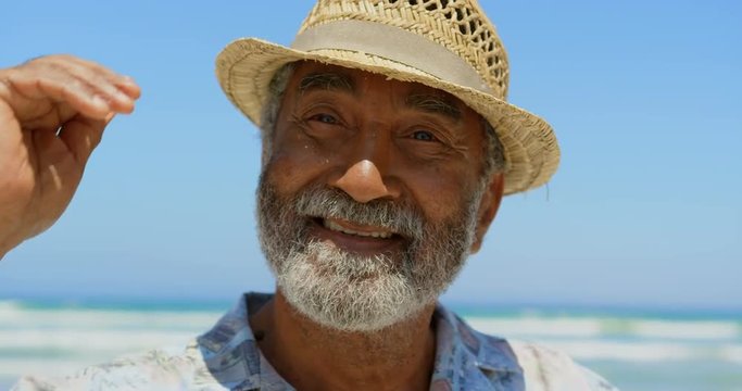 Front view of active senior African American man with hat standing on beach in the sunshine 4k