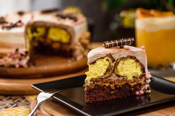 Beautiful chocolate layered cake with yellow filling and beautiful coffee glaze, decorated with tubules and pastry beads. Cake on a beautiful yellow background on a wooden table in the restaurant