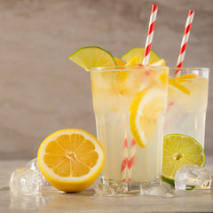 two glass of lemonade with lemons and lime and straw, on a dark background, with space, a cool drink and summer mood
