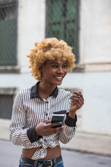 Young Black Stylish Woman Walking On The City Street  With A Smartphone