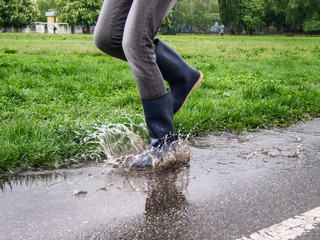 Girl in blue rubber boots jumps into a puddle in the stadium after the rain.