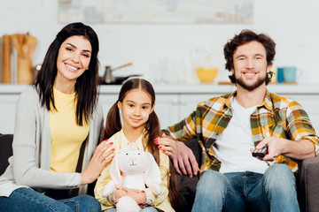 happy man holding remote controller near wife and daughter
