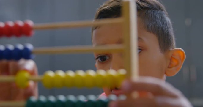 Front view of Asian schoolboy solving math problem with abacus at desk in a classroom at school 4k
