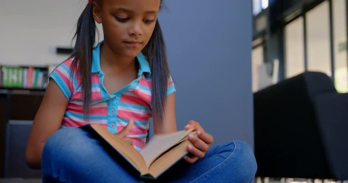 Front view of attentive African American schoolgirl reading a book in library at school 4k