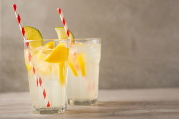 two glass of lemonade with lemons and lime and straw, on a dark background, with space, a cool drink and summer mood