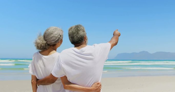 Rear view of active senior African American man pointing out at distance to woman at beach 4k