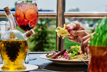 Man eats a fresh salad with vegetables and warm meat in a white plate on a dark glass table on a summer terrace. Close-up. Space