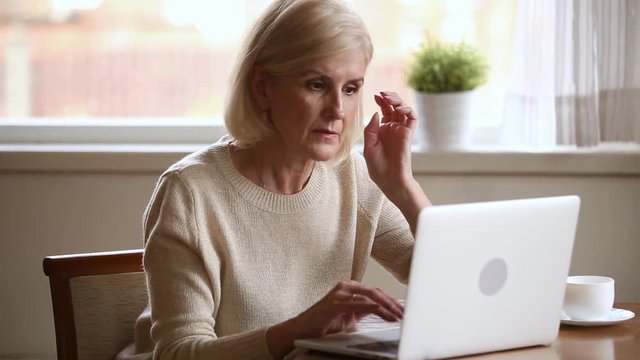 Serious elderly woman typing on computer working at home