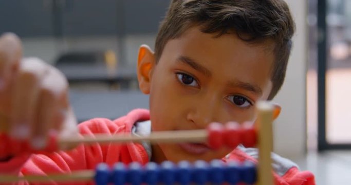 Front view of Asian schoolboy solving math problem with abacus at desk in a classroom at school 4k