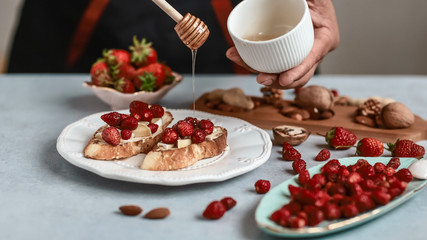 Cooking bruschetta sandwiches with strawberry, cheese and honey. Food recipe on wooden background. Flat top view from above