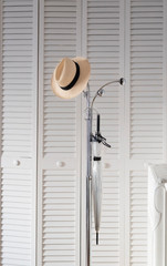 Un sombrero de paja y un paraguas en un perchero metálico sobre un fondo de puertas de madera lacades en blancor