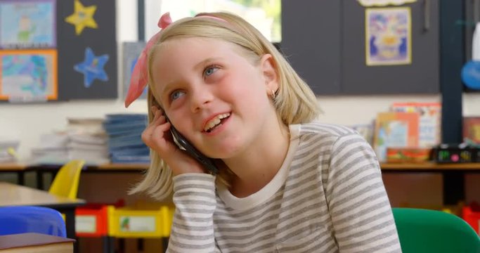 Front view of Caucasian schoolgirl talking on mobile phone at desk in classroom 4k