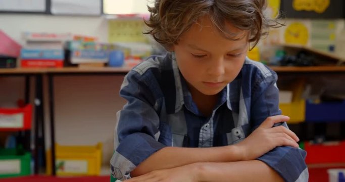Front view of Caucasian schoolboy studying on desk in classroom at school 4k