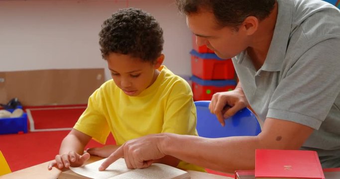 Front view of young Caucasian male teacher teaching African American schoolboy in classroom 4k