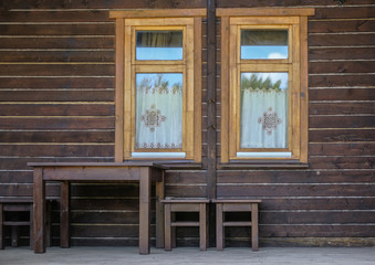 wooden brown facade of a vintage house with two Windows. wooden table and stools against the wal