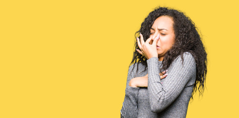 Young beautiful girl with curly hair smelling something stinky and disgusting, intolerable smell, holding breath with fingers on nose. Bad smells concept.