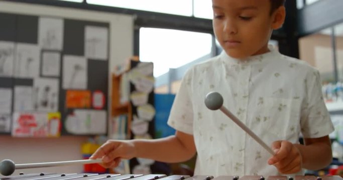 Front view of Asian schoolboy playing xylophone in a classroom at school 4k