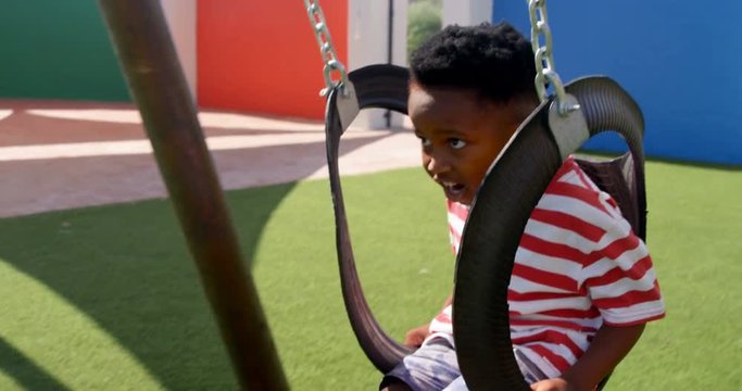 Side view of African American schoolboy playing on a swing in school playground 4k