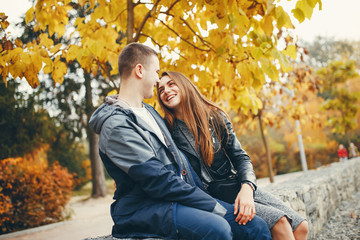 Cute couple sitting in a autumn park. Boy in a black jacket. Girl in a gray dress