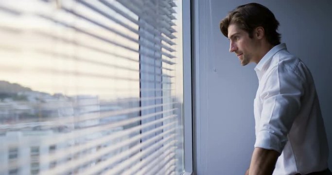 Side view of thoughtful young Caucasian male executive standing near window in modern office 4k