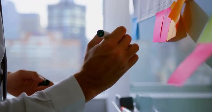 Mid section of young Caucasian male executive working on sticky note in a modern office 4k