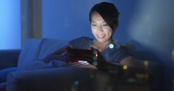 Woman play game on smart phone at home with window reflection