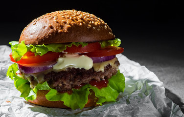 burger with meat, cheese and vegetables on dark black background