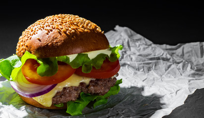 burger with meat, cheese and vegetables on dark black background