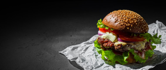 burger with meat, cheese and vegetables on dark black background