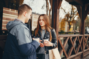 Cute couple standing near brown building. Boy and girl have fun in a autumn city. Couple drinking a coffee