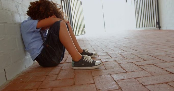 Side view of mixed-race schoolgirl sitting alone on the floor in corridor at school 4k