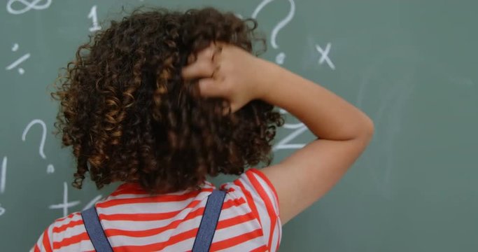 Rear view of mixed-race schoolgirl scratching her head in classroom at school 4k