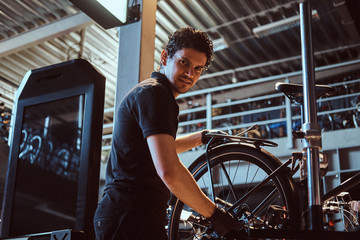 Fototapeta na wymiar Young attractive mechanic is fixing customer's bicycle at his own workshop.