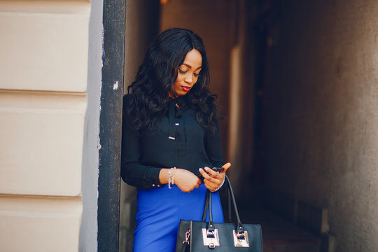 Elegant black woman standing in a summer city. Businesswoman in a blue pants
