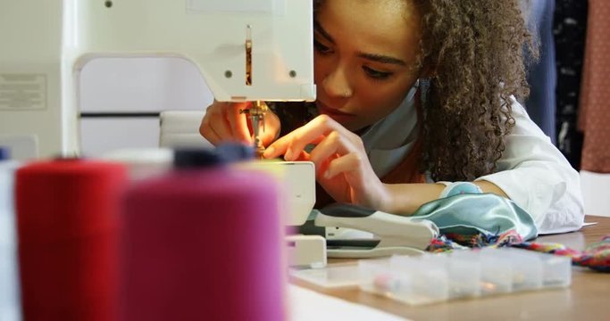Front view of African American female fashion designer working with sewing machine in workshop