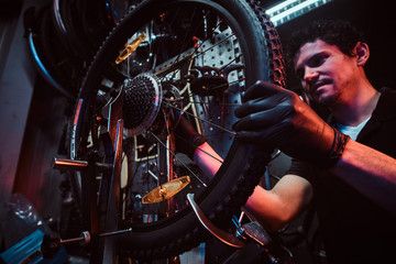 Diligent attractive mechanic is fixing bicycle at his own workshop.