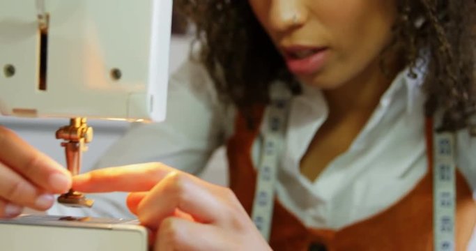 Front view of African American female fashion designer working with sewing machine in workshop