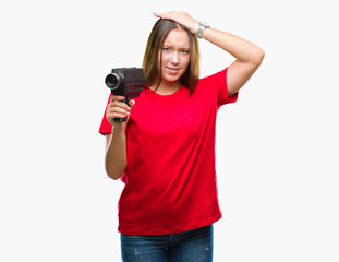 Young beautiful caucasian woman filming using vintage video camera over isolated background stressed with hand on head, shocked with shame and surprise face, angry and frustrated. Fear and upset