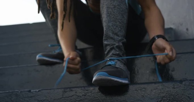 Front view of young African American woman tying shoelaces in the city 4k
