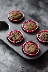 Tasty homemade chocolate muffins in baking tin on dark monochrome background