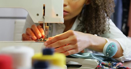 Front view of African American female fashion designer working with sewing machine in workshop
