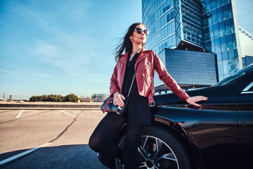 Young attractive woman is chilling in bright sunny day next to her car.