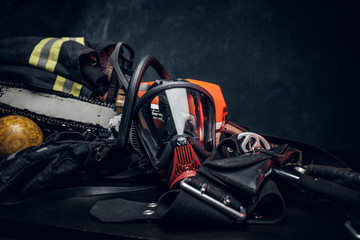 Fototapeta premium Bezpieczeństwo na stole - kurtka i rękawiczki z butlą tlenową, respirator i piłą łańcuchową. Istnieje ciemne tło.