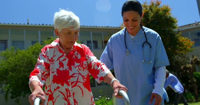 Front view of female doctor helping senior patient to walk with walker in the garden of nu